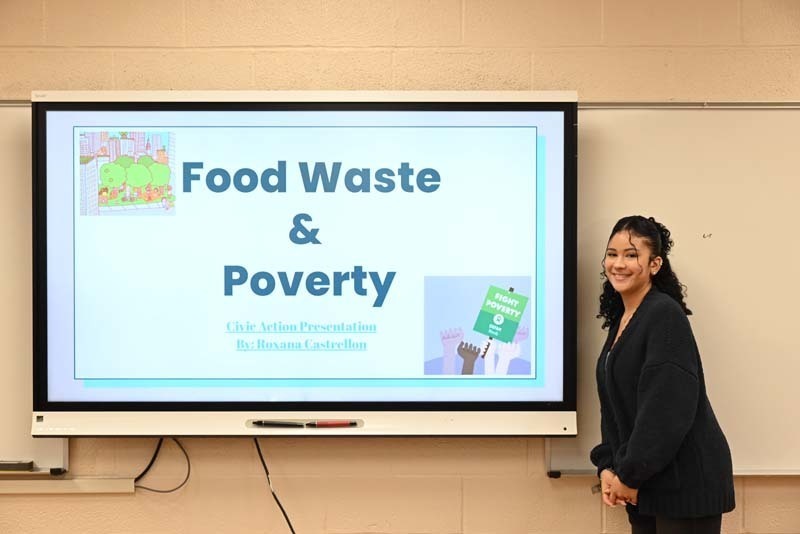 A person standing next to a SmartBoard with the words Food Waste and Poverty