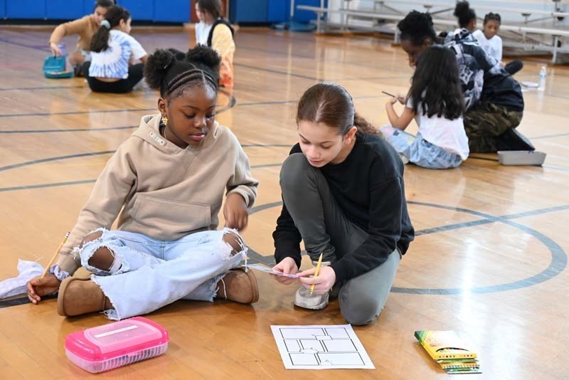 Two people sitting on the gym floor and working on a worksheet