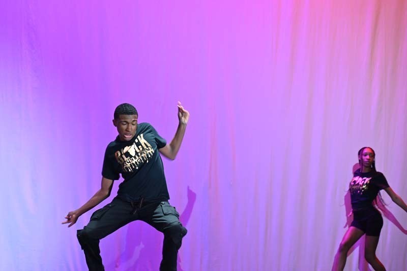 Students dancing on a stage light up in pink and purple