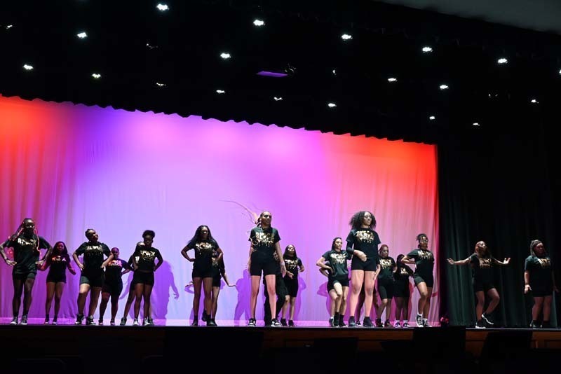 Students dancing on a stage light up in pink and purple