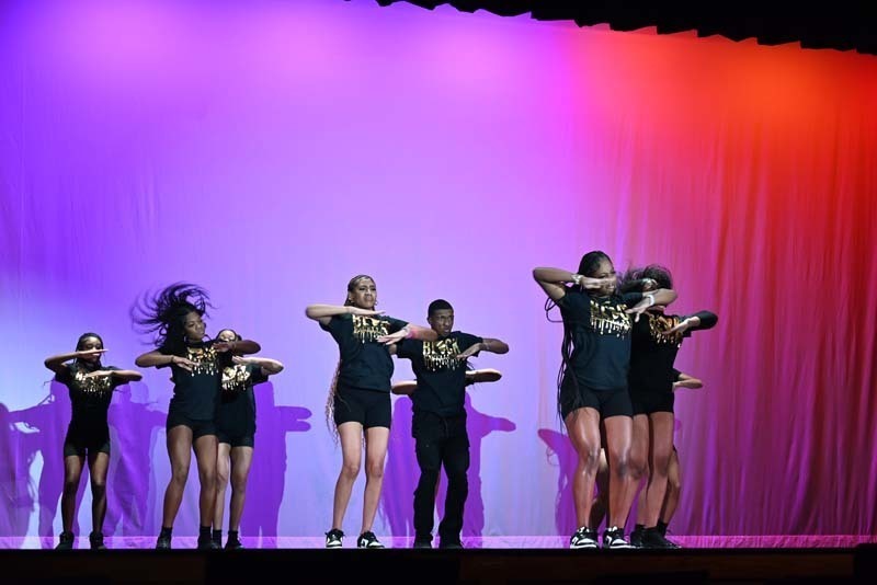 Students dancing on a stage light up in pink and purple