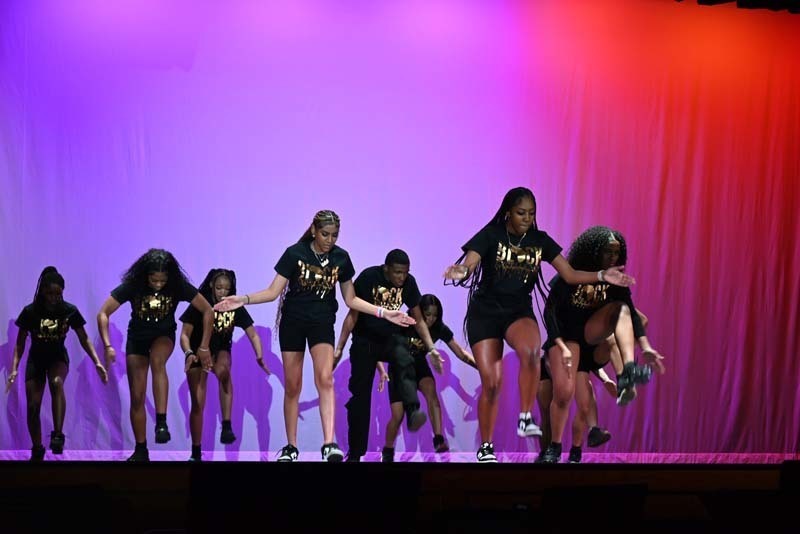 Students dancing on a stage light up in pink and purple