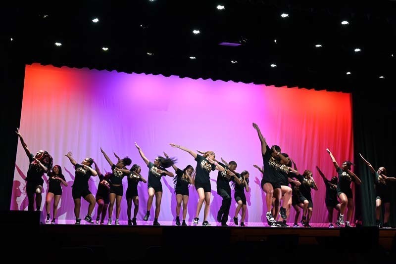 Students dancing on a stage light up in pink and purple