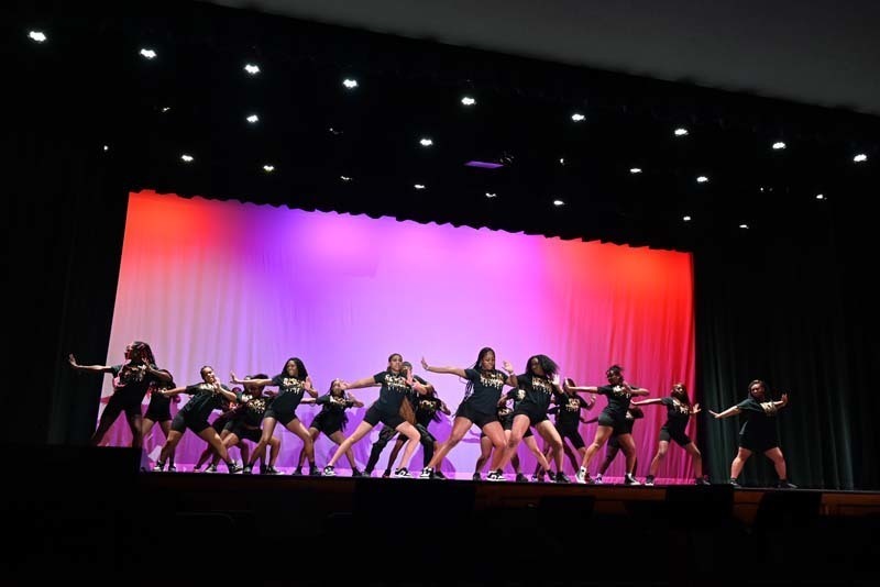 Students dancing on a stage light up in pink and purple