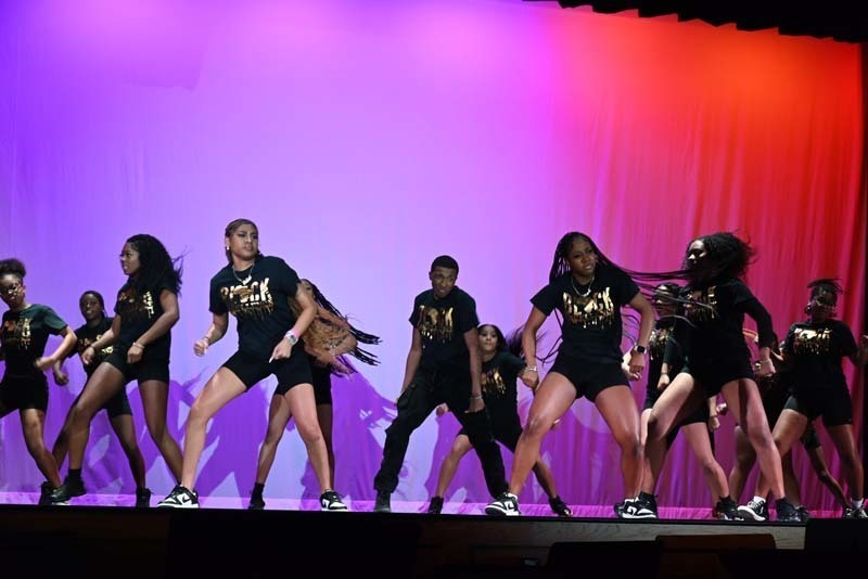 Students dancing on a stage light up in pink and purple